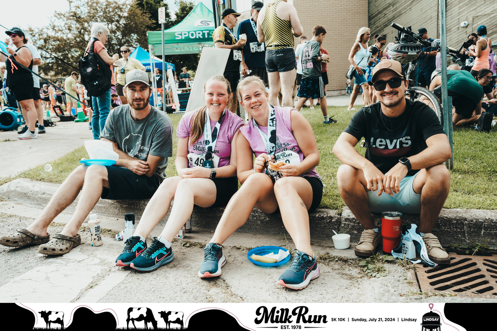 Runners pose for a group photo while sitting on the curb.