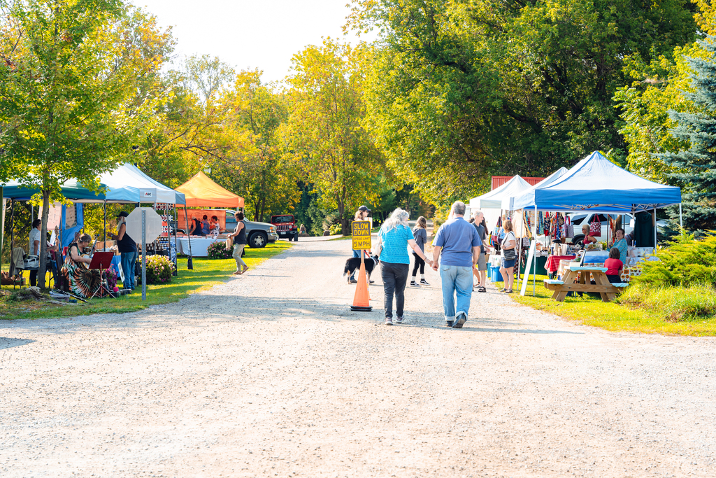 People walk along a road with vendor tents on both sides.