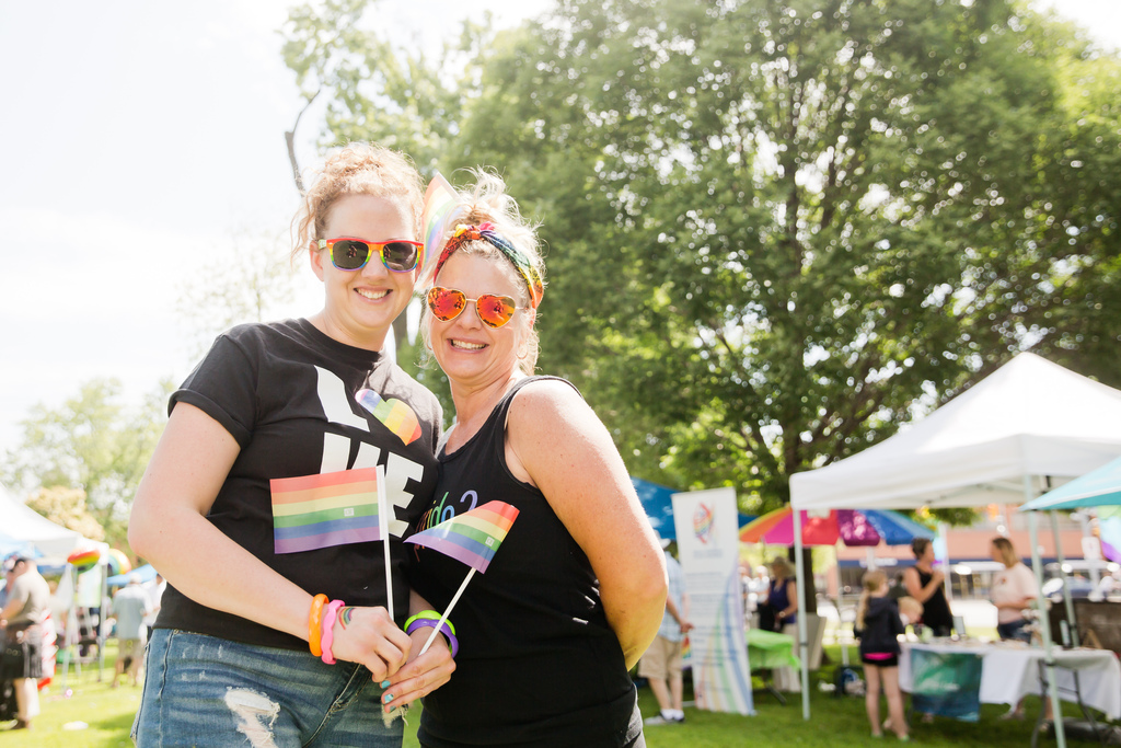 Two females wearing black shirts smile and hold Pride flags.