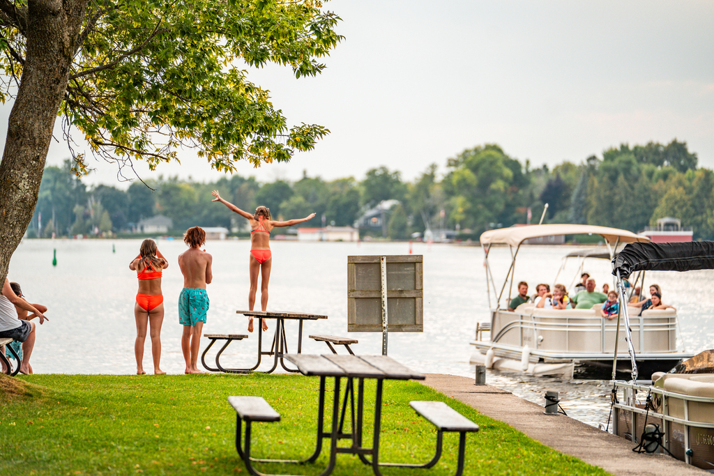 Children jump off a dock into a lake.